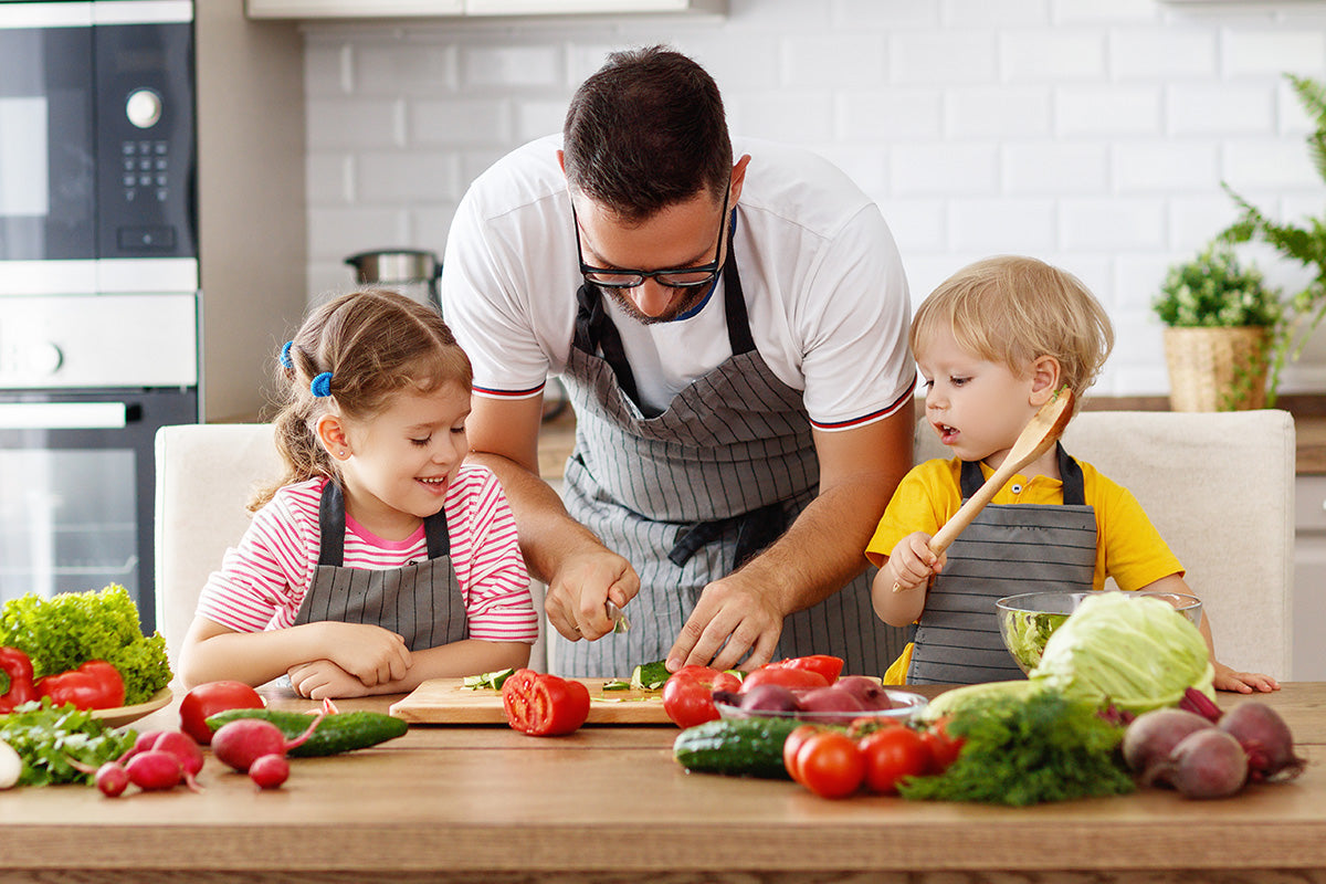 Father cooking with children in kitchen preparing vegetables