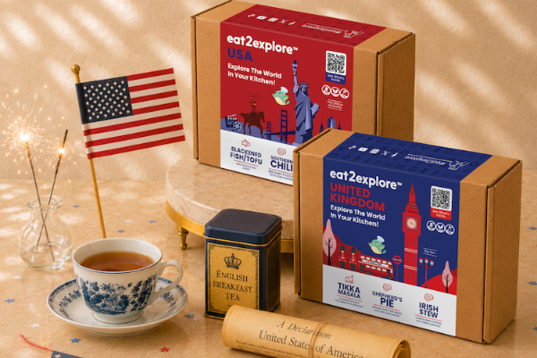 eat2explore USA and United Kingdom themed tea boxes with a cup of tea and American flag on a wooden surface.