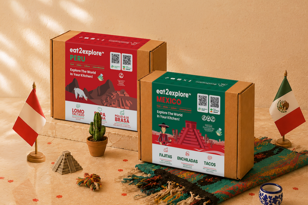 Two branded cardboard boxes for eat2explore travel food experiences are displayed on a warm beige surface with decorative props. The larger red box says PERU and the smaller green box says MEXICO, both with QR codes and food imagery.