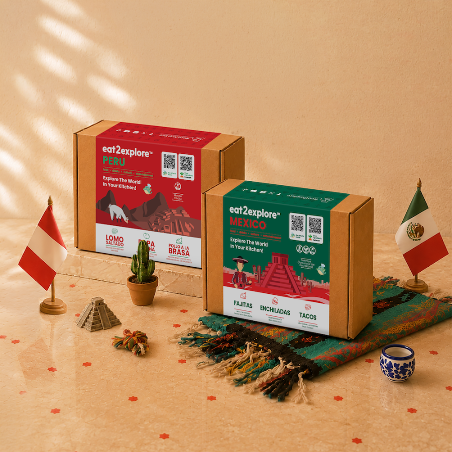 Two branded cardboard boxes for eat2explore travel food experiences are displayed on a warm beige surface with decorative props. The larger red box says PERU and the smaller green box says MEXICO, both with QR codes and food imagery.