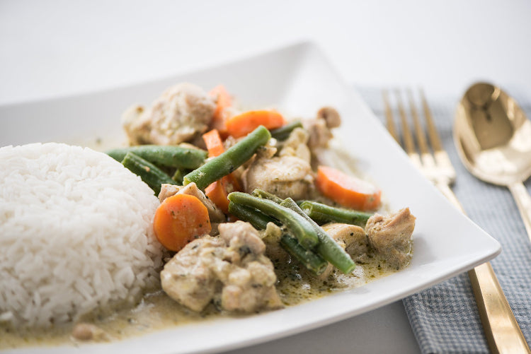 Thai green curry with chicken, vegetables, and rice on a white plate.