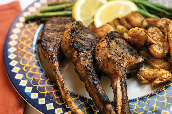 Grilled lamb chops on a decorative plate with lemon slices and green beans.